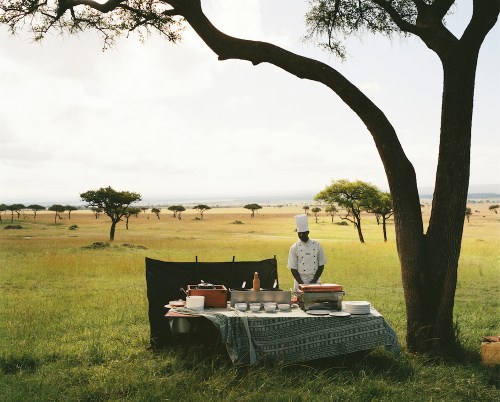 A chef from a nearby luxury lodge waits for his guests to arrive from a hot air balloon excursion before serving them champagne in the middle of the Maasai Mara National Reserve, Kenya. 2012 Guillaume Bonn